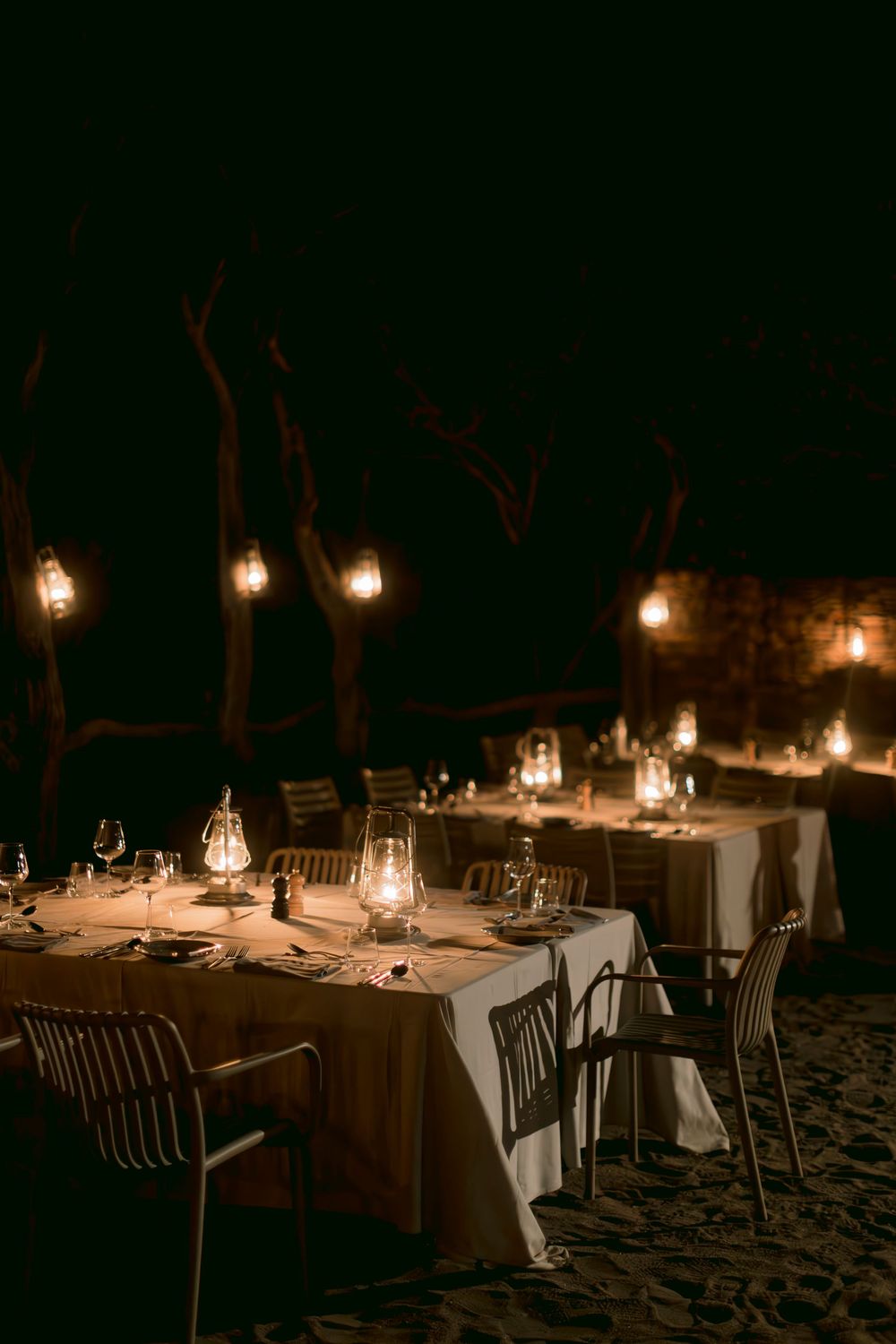 Romantic outdoor night dining setup with glowing lanterns and string lights illuminating white tablecloths.