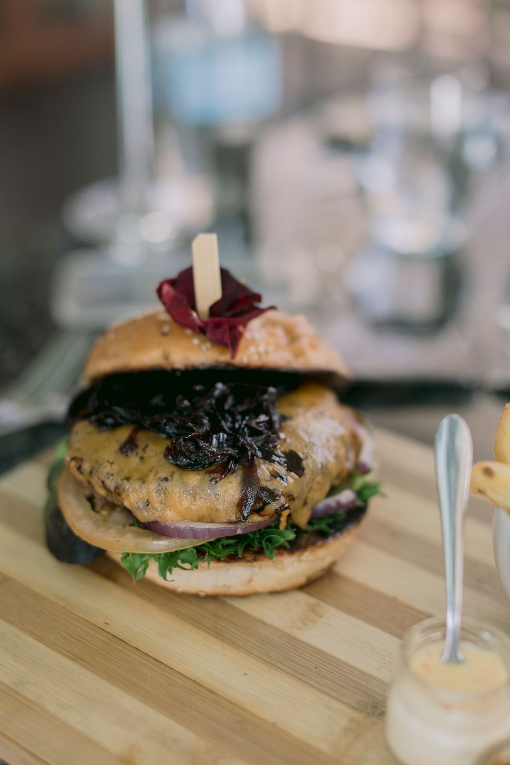 Gourmet burger with caramelized onions on wooden board served with dipping sauce at restaurant.