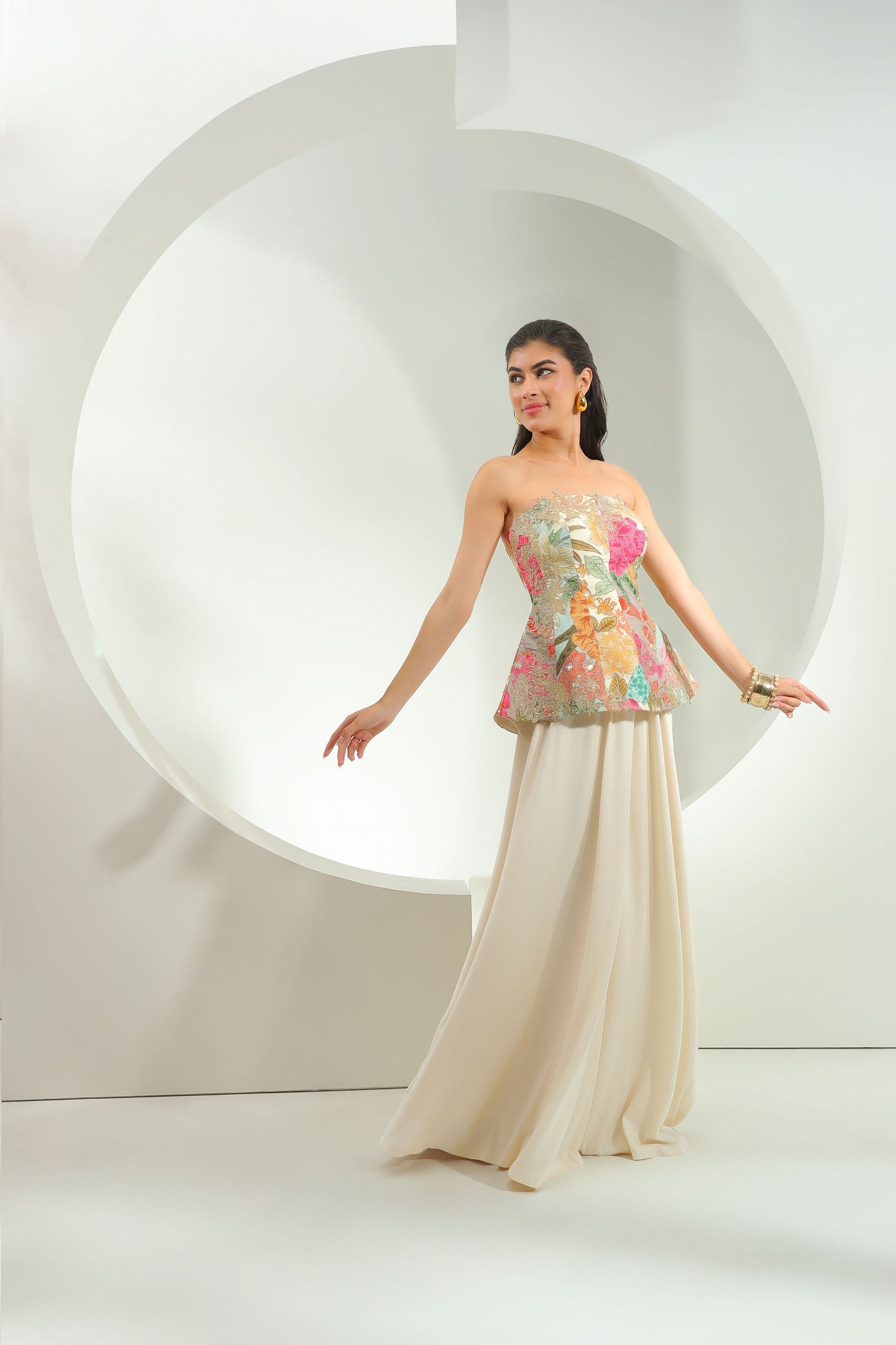 A floral crop top and beige maxi skirt ensemble shown in a white studio setting with curved architectural details.