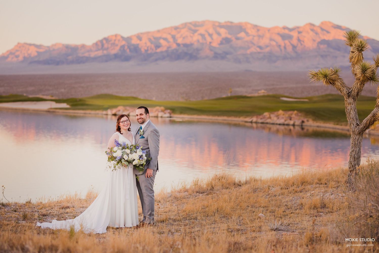 A couple shares a romantic moment in front of a scenic desert landscape with rocky outcrops and lush greenery.