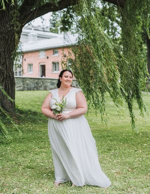 A bride in a flowing white dress poses under a weeping willow tree.