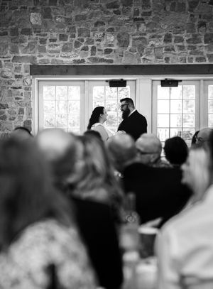 A black and white panoramic shot of a wedding ceremony in a rustic stone venue.