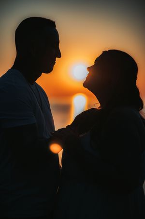 Romantic silhouette of a couple facing each other against a golden sunset over the ocean.