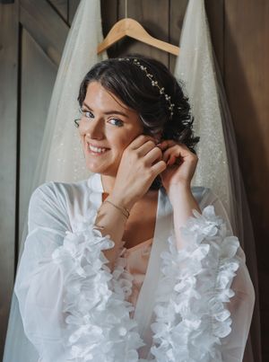 A bride in white ruffled sleeves adjusts her earring while getting ready.