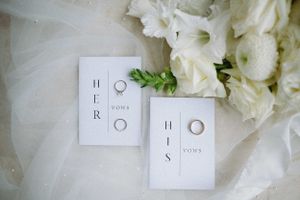 Wedding rings and minimalist invitation cards displayed with white flowers.