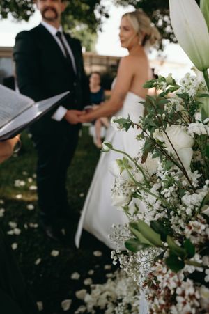 Wedding ceremony with white floral arrangements and greenery in the foreground.