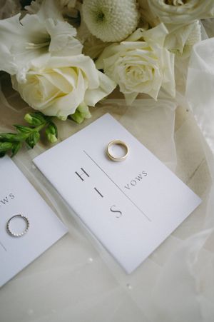 Wedding invitation and rings styled with white roses and classic typography.