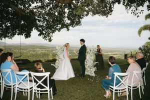Wedding ceremony overlooking valley with guests seated in white chairs.
