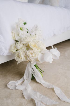 Elegant white rose bouquet with flowing silk ribbons against a light background.