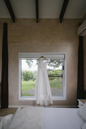 White wedding dress hanging in window frame with natural light streaming in.