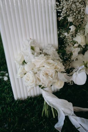 Elegant white rose wedding bouquet with ribbon rests against column.
