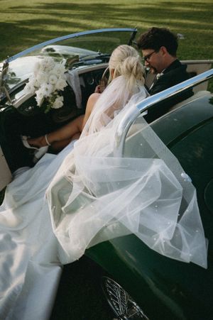 Couple in vintage convertible car with flowing wedding veil.