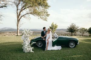 Classic vintage car adorned with floral decorations against a scenic countryside backdrop.