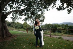 Couple embracing under large tree with mountains in background.