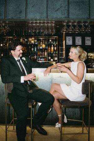 A couple sharing drinks at a stylish bar with glassware displayed overhead.