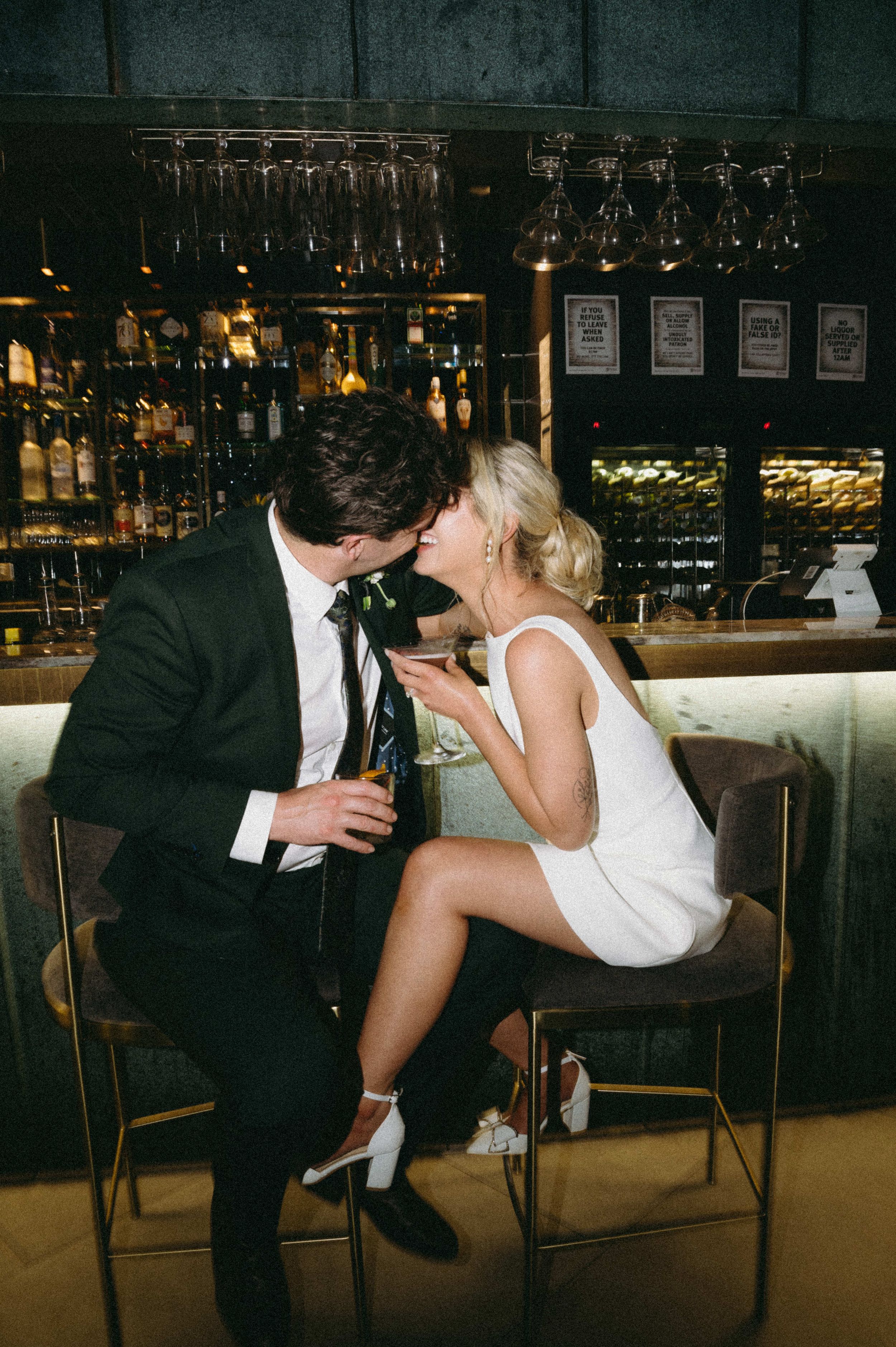 Intimate moment captured at an elegant bar with hanging wine glasses in the background.