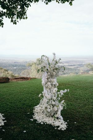 Elegant white floral wedding arch arrangement on hillside with valley views.