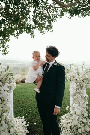 Outdoor wedding ceremony setup with white floral arch and scenic mountain backdrop.