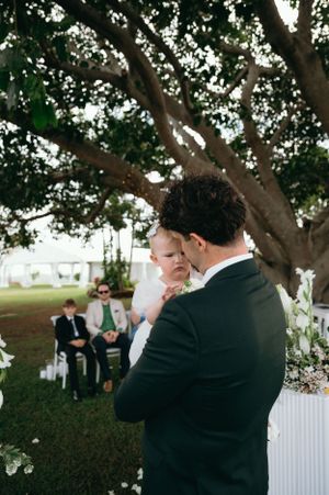 Intimate wedding ceremony moment under a large tree with white floral decorations.