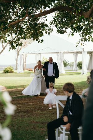 Wedding ceremony processional under white tent with guests seated on white chairs.