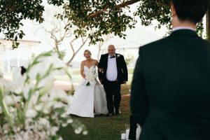 Scenic outdoor wedding ceremony with white tent and floral decorations.