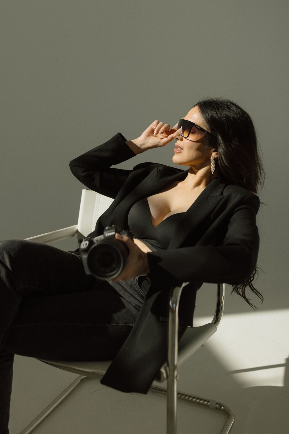 Dramatic fashion portrait series showing a person in black blazer reclining on chair with strong shadows and lighting.