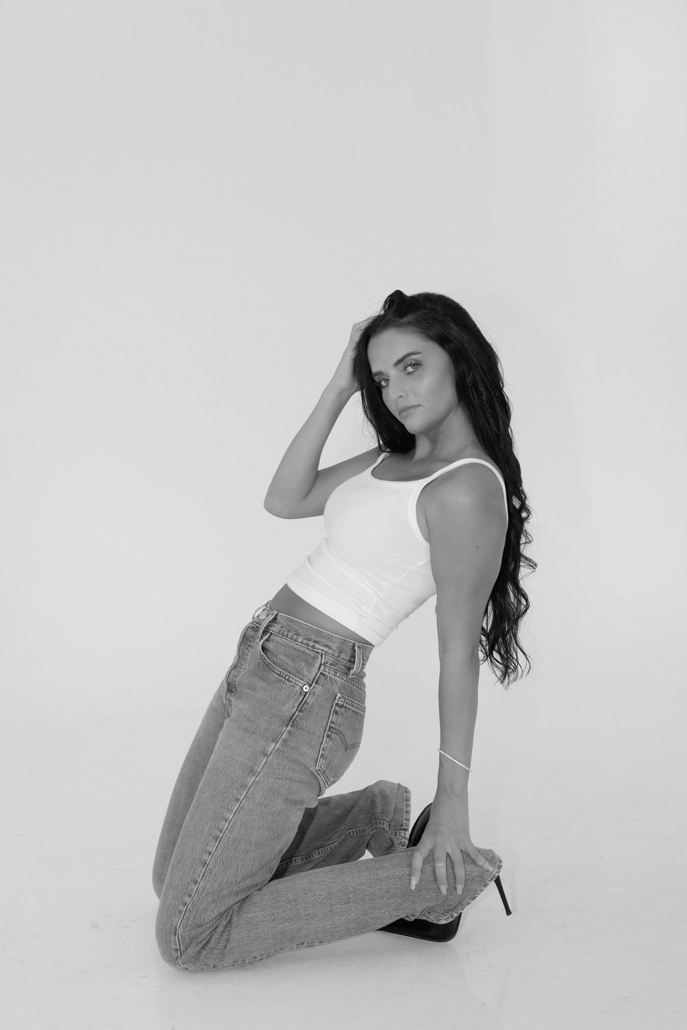 A series of four artistic black and white fashion photos showing a model in a white tank top and light denim jeans.
