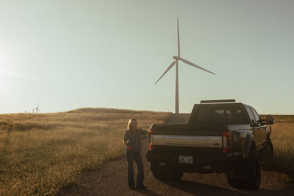 Wind turbine installation crew works in an open field during golden hour as sun sets behind distant hills.
