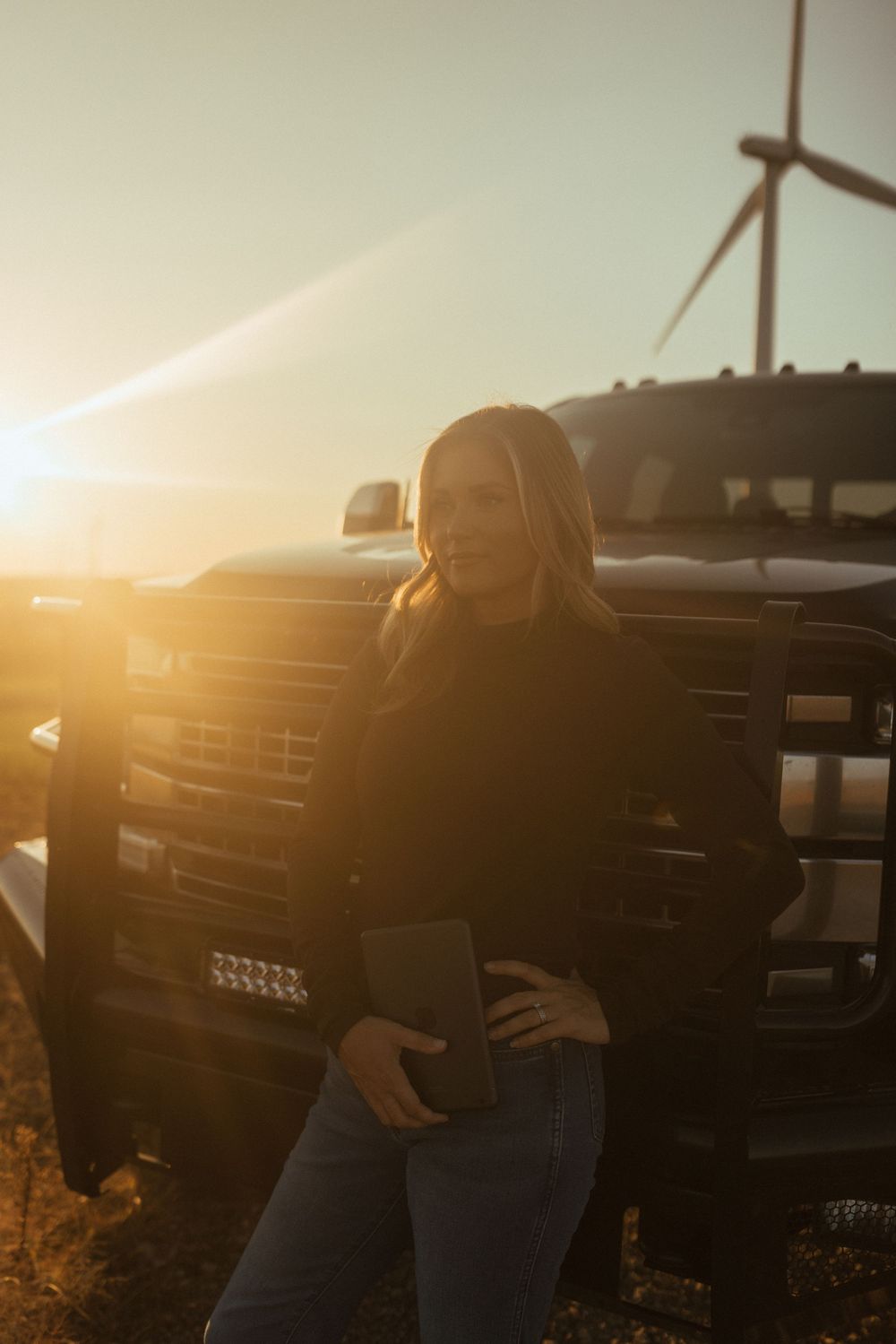 A silhouetted figure stands against a warm sunset sky with lens flare and industrial equipment in the background.