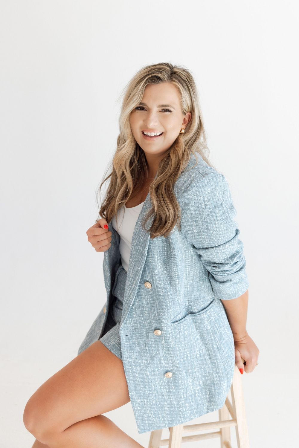 Fashion model wearing light blue textured blazer poses against white background in studio photoshoot.