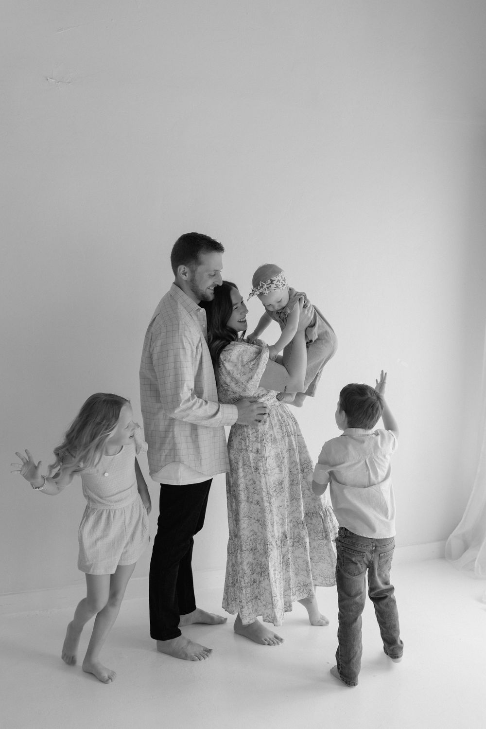 Four black and white photos show a family group in matching light-colored outfits posing playfully against a white backdrop.