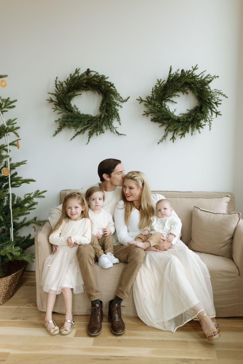 A series of four minimalist family portraits showing people sitting on a beige couch against a white wall with evergreen decor.