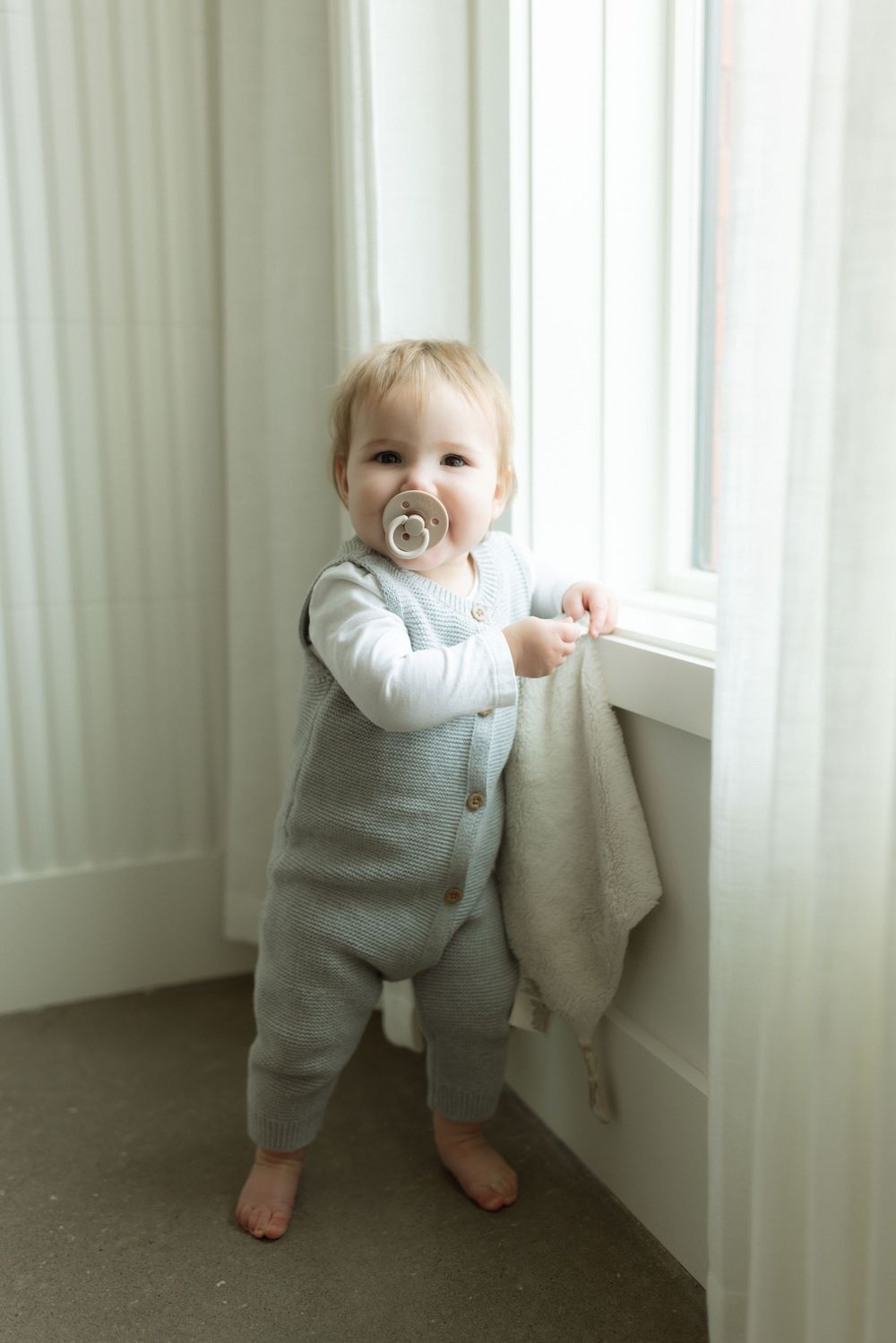 A toddler in gray overalls and white shirt stands by a window, creating a series of three progressive images.