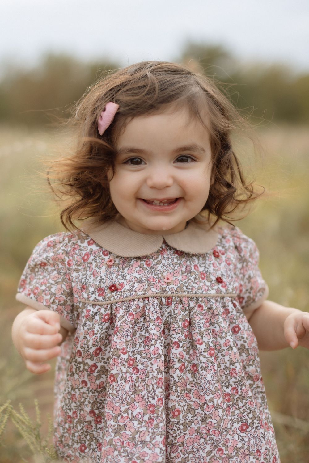 A small child in a floral print dress plays outdoors in a natural field setting.