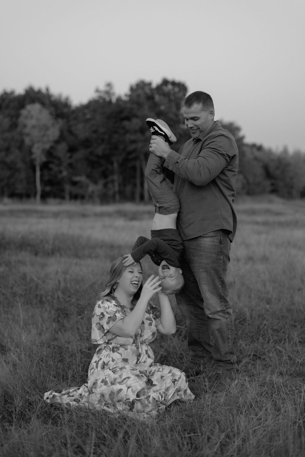 A couple sits together in a grassy meadow on a romantic black and white photoshoot.