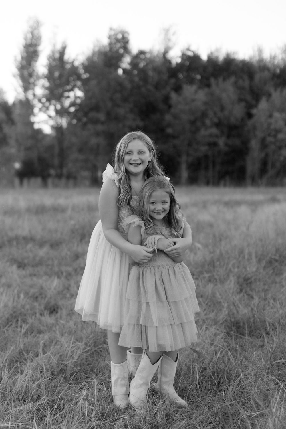 Black and white photo series showing two people in white dresses embracing in a grassy field.