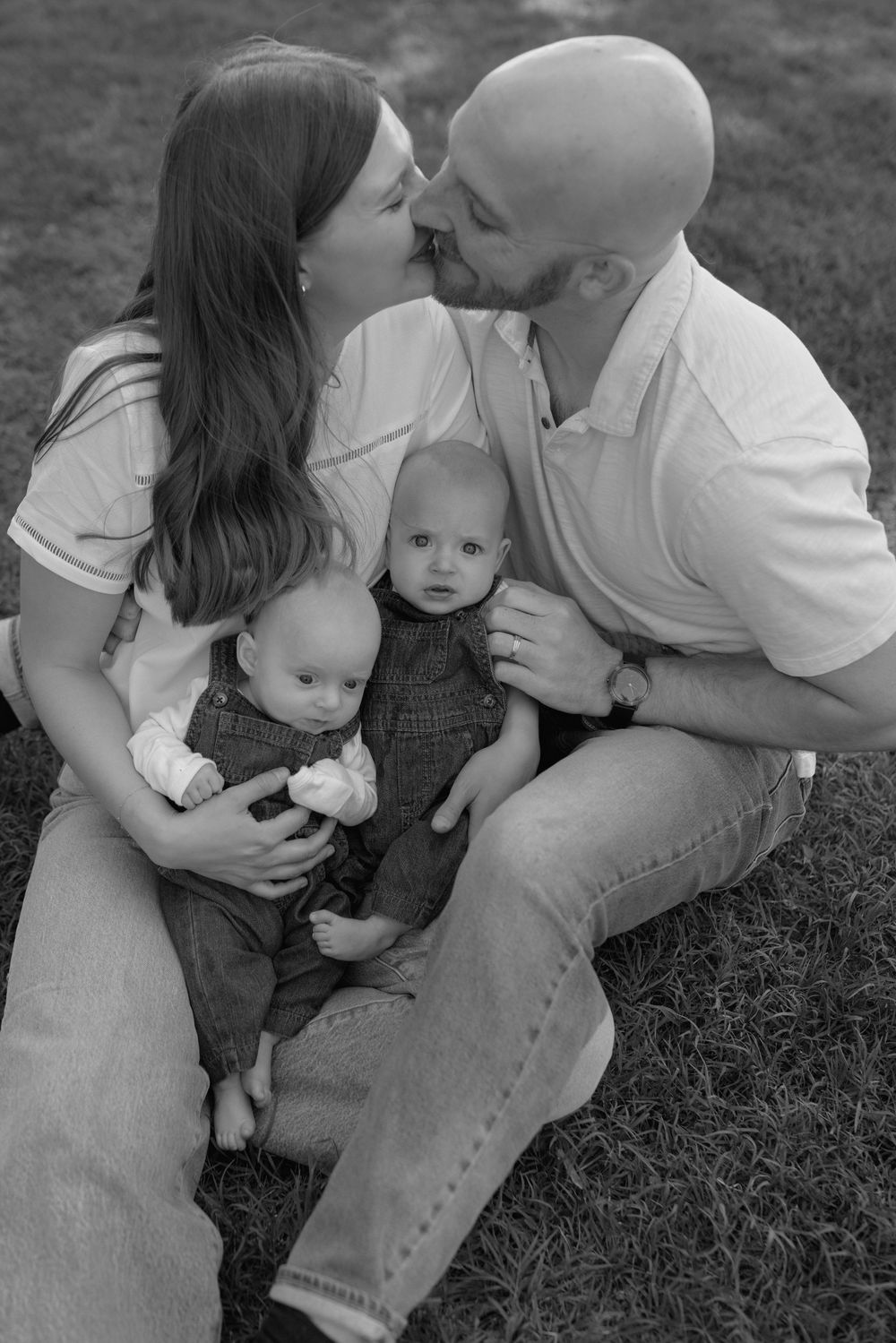 A series of black and white intimate family photos showing tender moments between parents and baby on grass.
