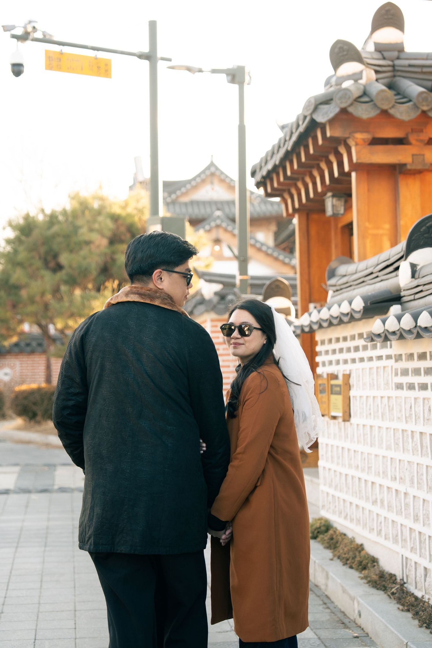 Two people in warm coats walking along a traditional Korean palace wall during autumn.