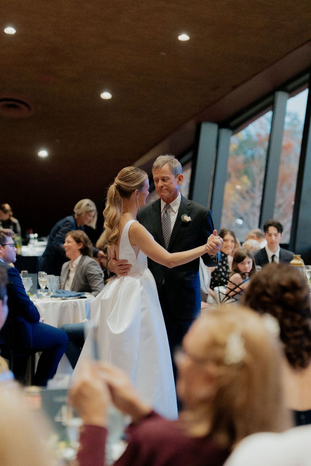 A couple shares their first dance at a wedding reception while guests look on from their tables.