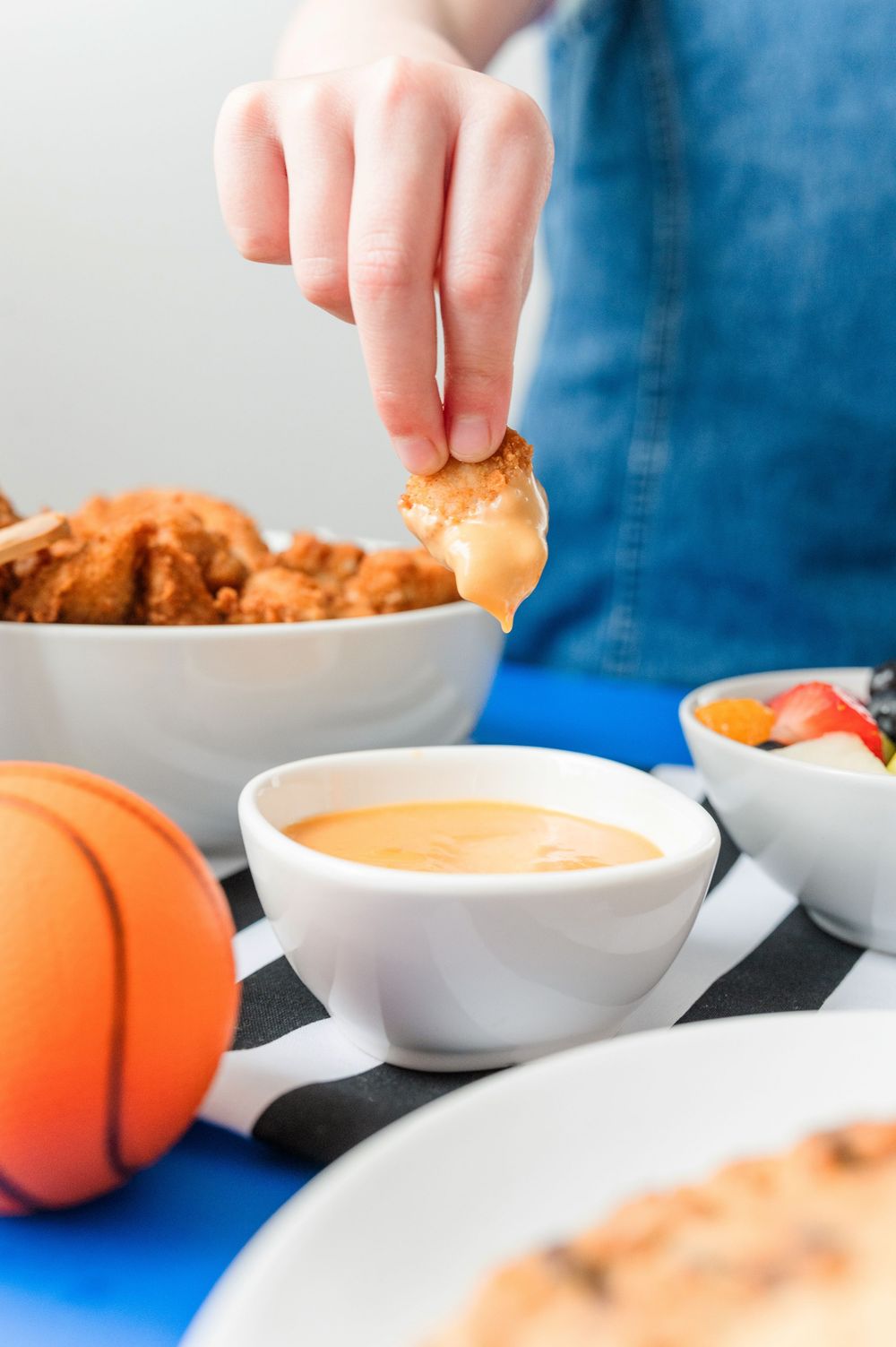 Dipping sauce in white bowls with chicken tenders and orange decorations.
