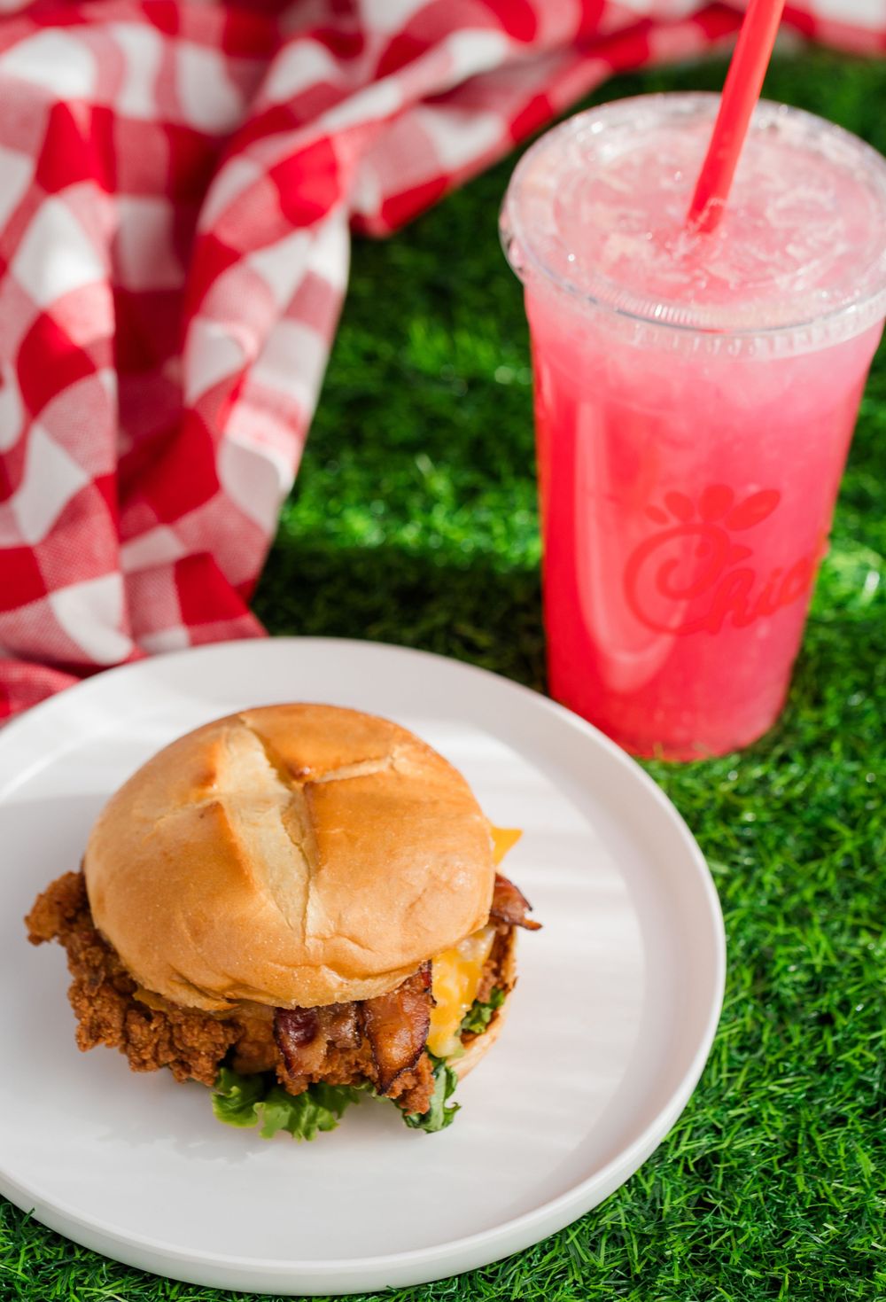 Chicken sandwiches on white plates with pink beverages against a red and white checkered background.