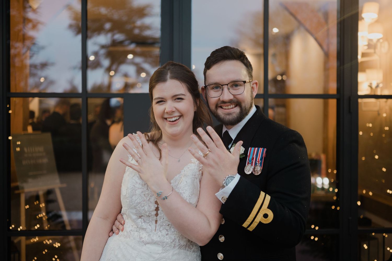 A couple shares a joyful moment during their wedding reception with city lights visible through windows in the background.