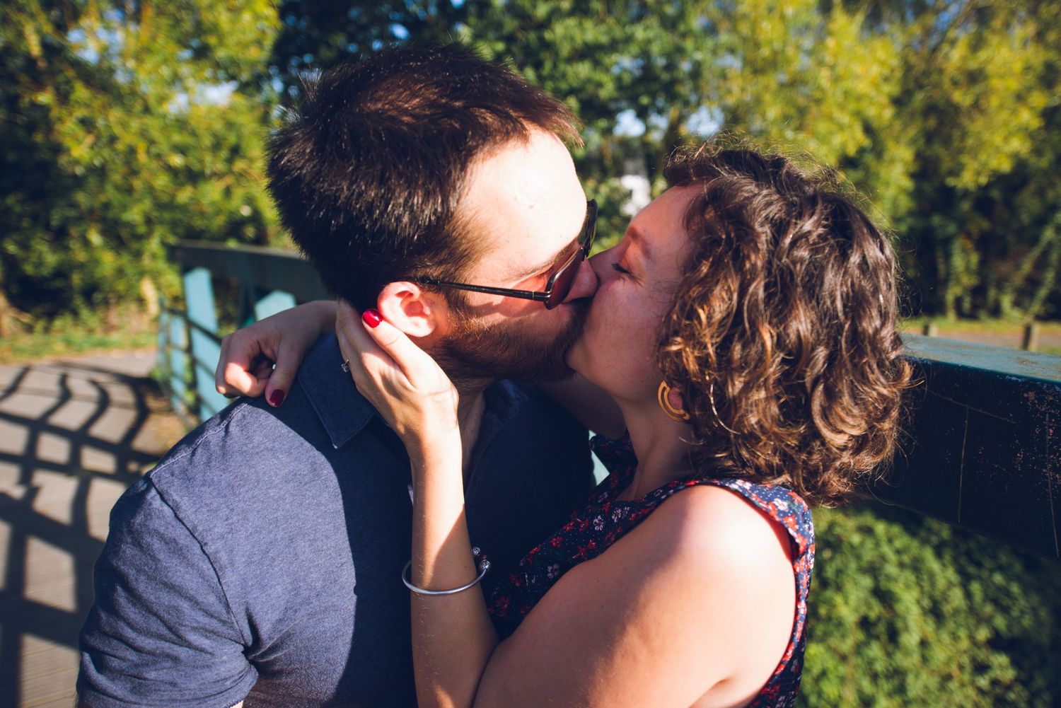 Couple échangeant un baiser tendre dans un parc ensoleillé lors d’une séance engagement.