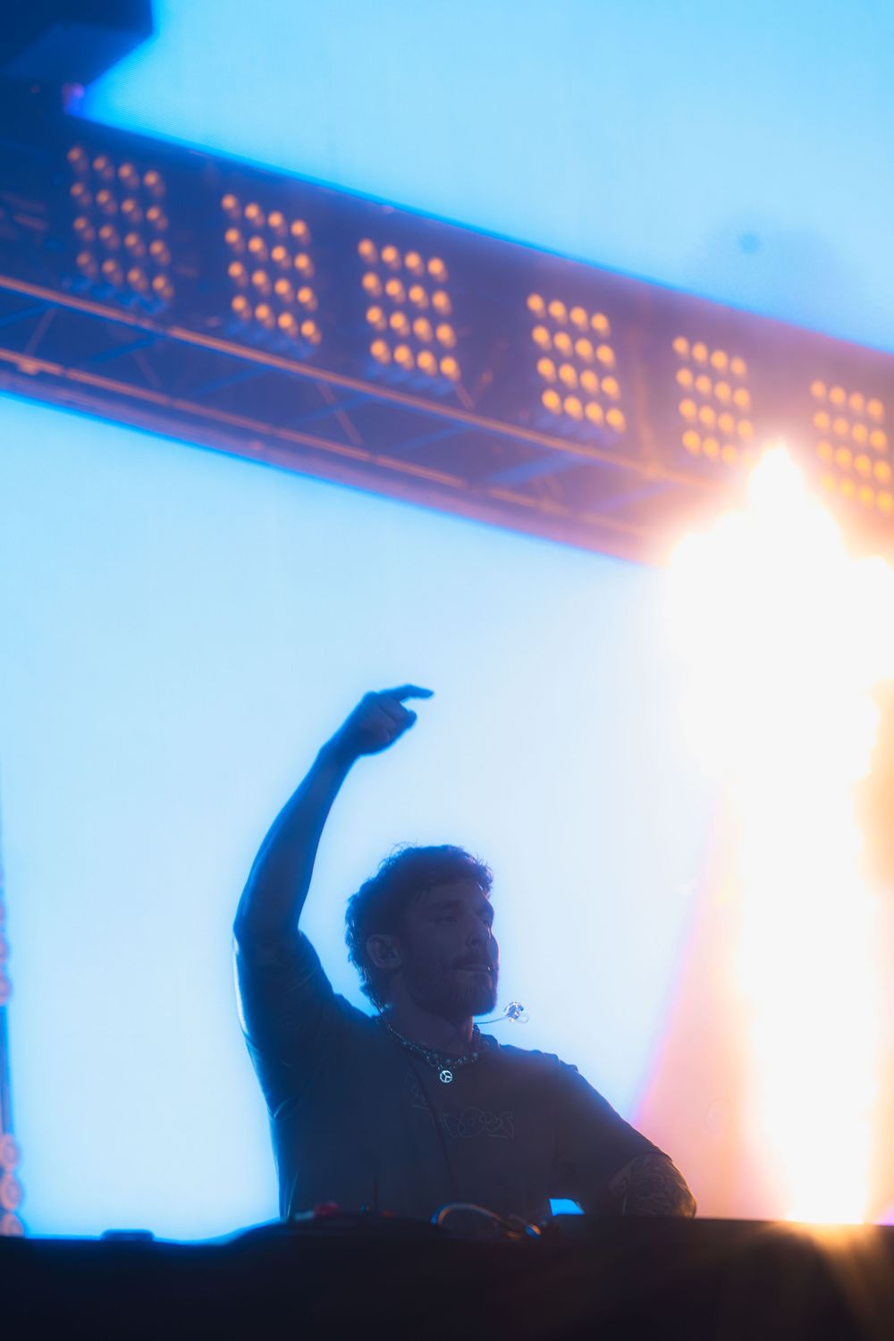 A silhouetted DJ performs on stage with dramatic blue lighting and LED panels creating an atmospheric concert scene.