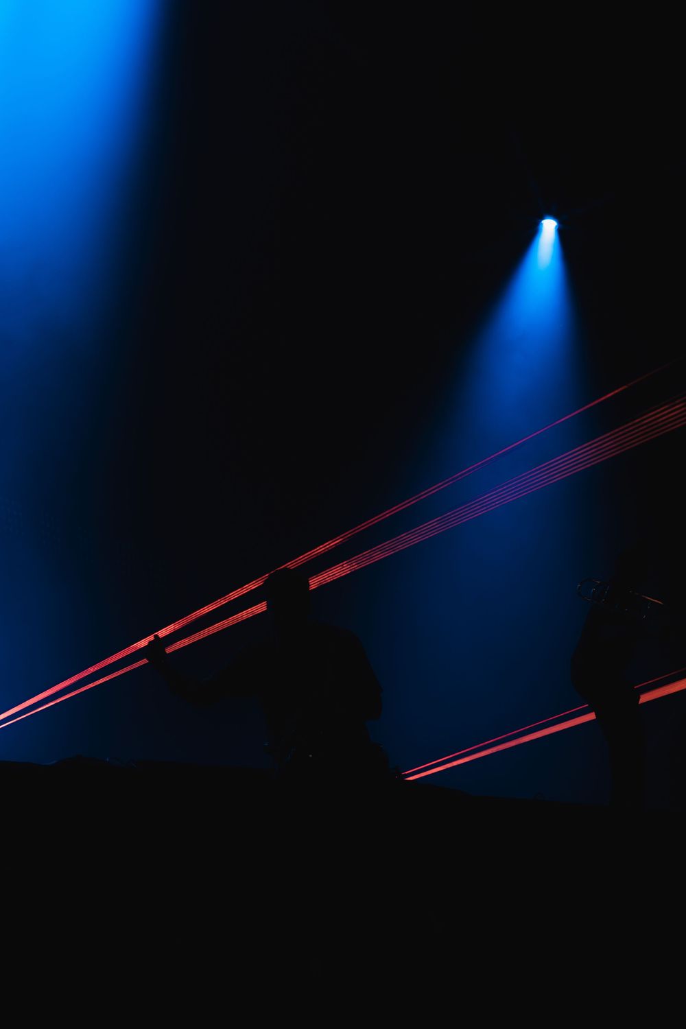 Blue spotlights illuminate red laser beams cutting through darkness in a dramatic stage lighting display.