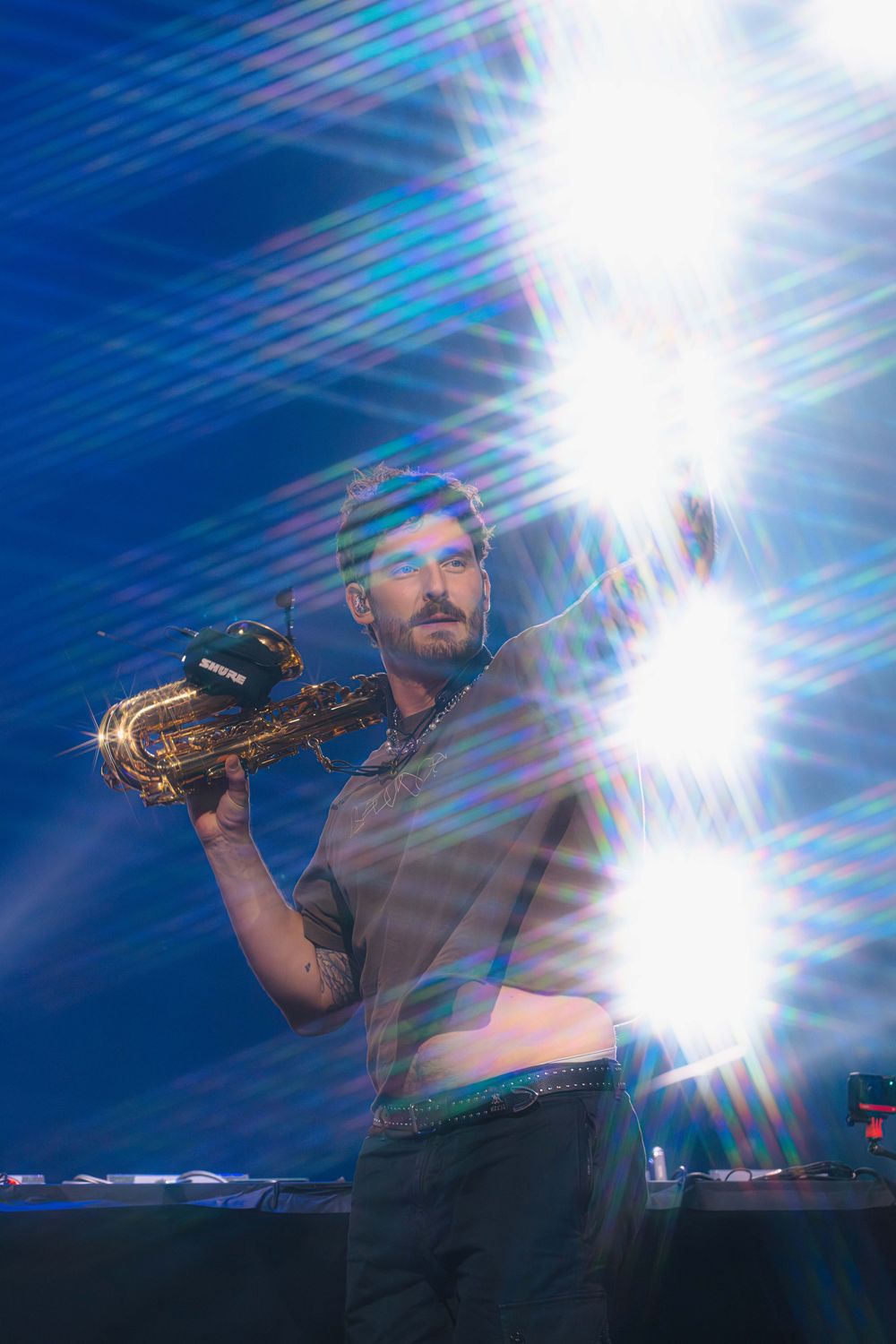 A musician performs on stage with a saxophone under dramatic blue lighting and lens flares.