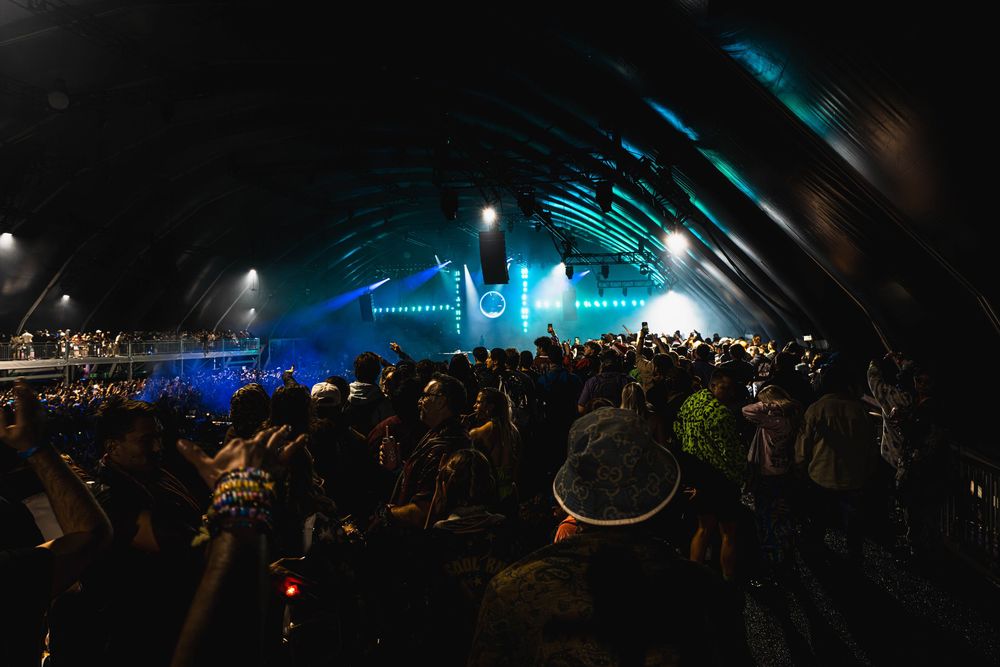 Concert crowd silhouettes against dark background with blue stage lighting creating atmospheric ambiance.