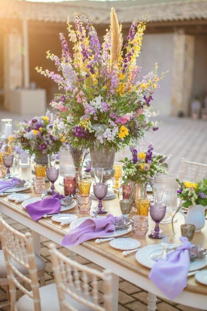 Elegant outdoor wedding table with purple floral centerpiece and colorful glassware.