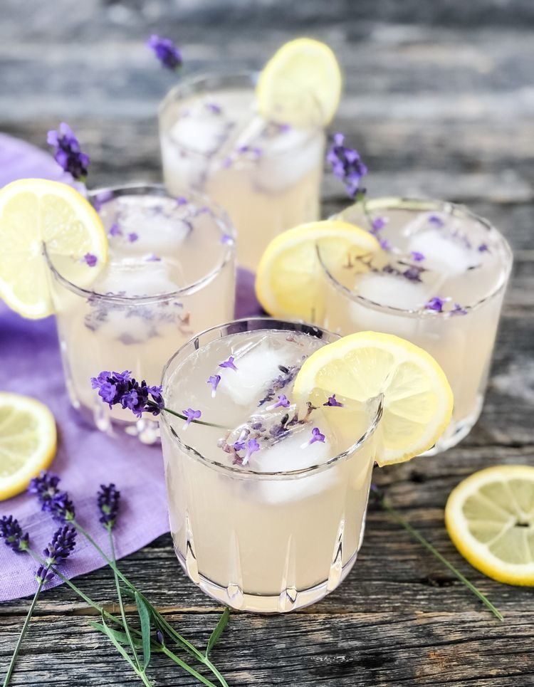 Refreshing lavender lemonade cocktails garnished with lemon slices and fresh lavender sprigs on rustic wood.