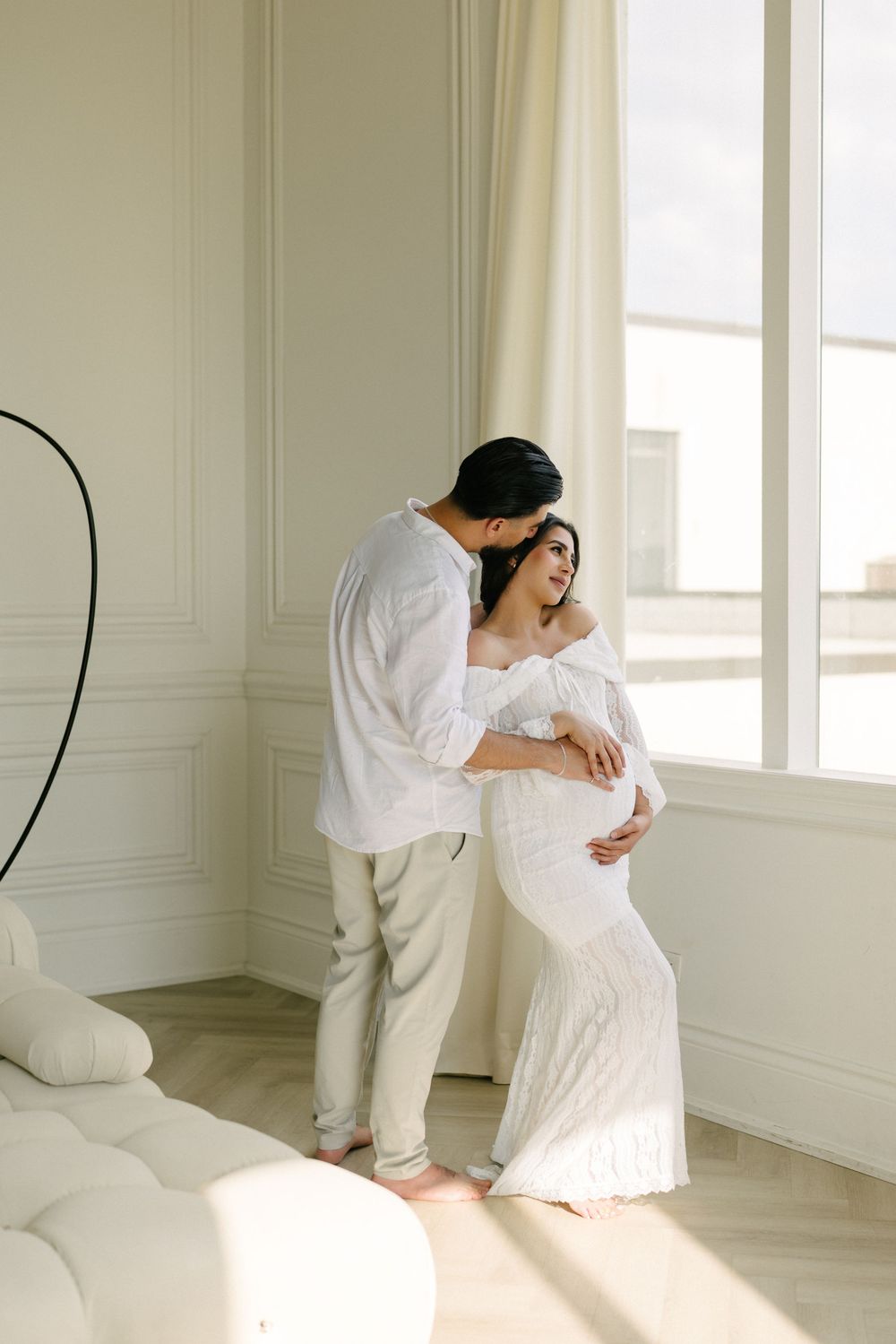 Expectant couple standing forehead to forehead in a bright room.